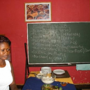 Evelyne devant le menu: loso, makemba; fufu, mosaka, makayambu, pondu
